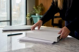 Na biurku w gabinecie ląduje teczka z ważnymi dokumentami prawnymi, którą ktoś właśnie odkłada ręką.